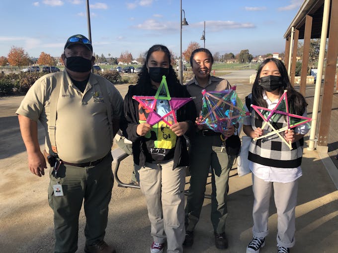 Asian male and female park rangers in uniform with two teenage asian girls holding colorful paper and wood lanterns in the shape of a star.