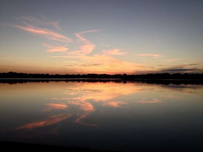 The sun sets over Lake Harriet. The clear surface of the lake mirrors the pink clouds.