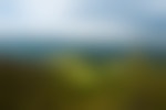 A greenery-covered mountain with green and blue mountain ridges in the distance and gray clouds in the sky.