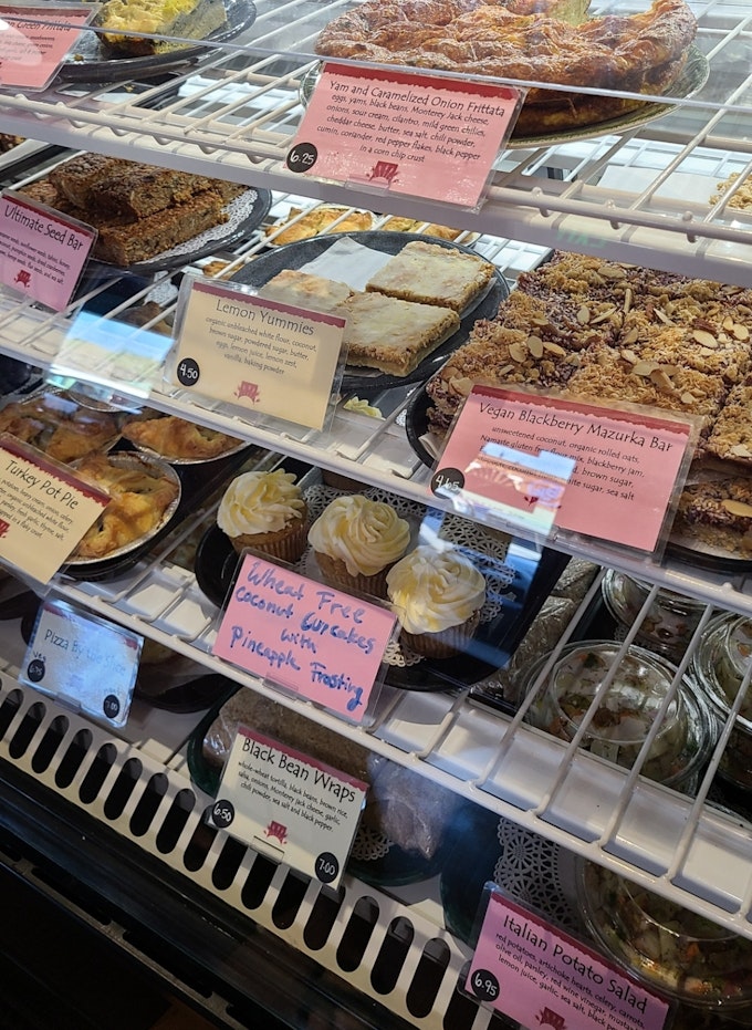 A bakery case full of cupcakes, bars, muffins, and pies. Each item is labeled with ingredients.