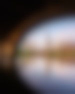 The view from under a bridge on a lake. There is another bridge in the background and a city skyline. The water is calm and reflects the surroundings.