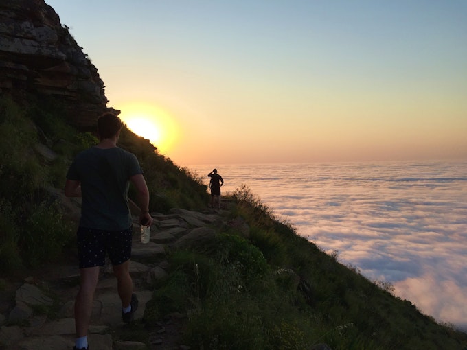 clouds at sunset surrounding mountain top with two hikers