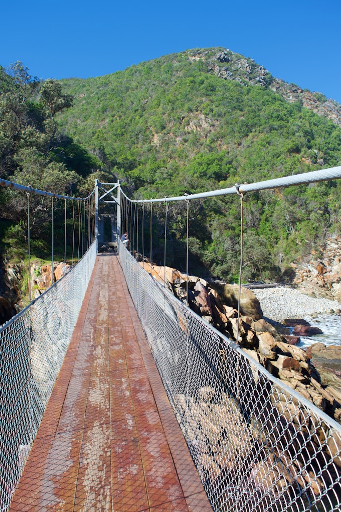 Suspension bridge over a river with green hill behind