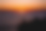 The sun is setting on the Pacific Ocean casting bright, orange light into the sky. Silhouetted onlookers enjoy the view atop a bluff.