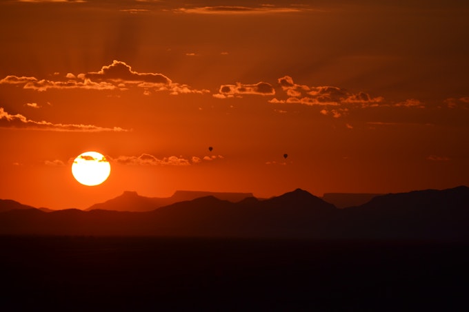 Orange sun rising up with shadows of sand dunes and two hot air balloons