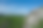 A lone hiker sits atop the rocky cliff outcropping looking at the bright green forest below