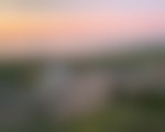 A hiker looks out over a green coated valley as clouds roll through and the sun turns the sky light pink