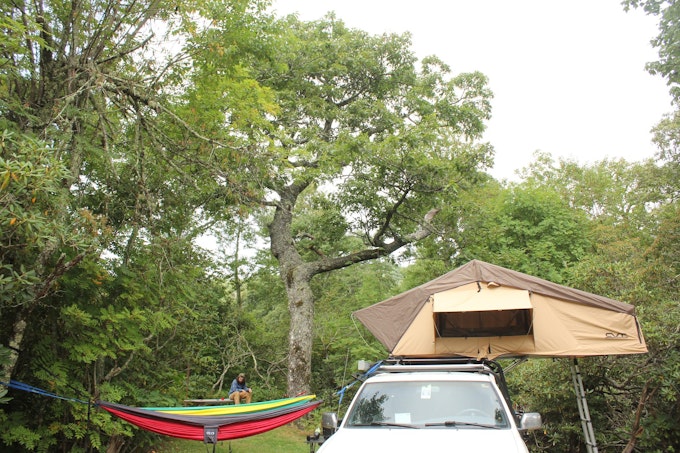 A car has a tent set up on top of it and a hammock attached to it