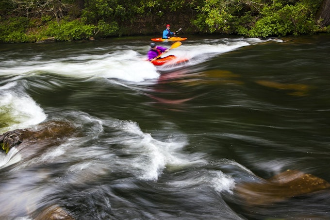 Two kayakers maneuver through the river rapids
