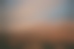 Clouds sit just above Sierra Nevada mountains, colored red by the rising sun. There is a wooden, old building sitting wtihin the sagescrub desert floor.