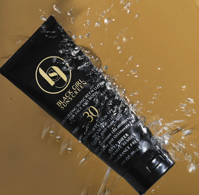 A product shot of a black sunscreen container with a yellow background and water bouncing off the container.