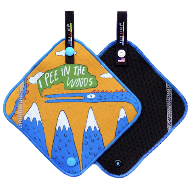 A rectangular piece of fabric with rounded corners featuring a drawing of a bluish creature and blue mountains with snow. There is a green blob that reads, 