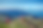 3 hikers walk along a trail with a view of the blue ocean and green hills in the background.