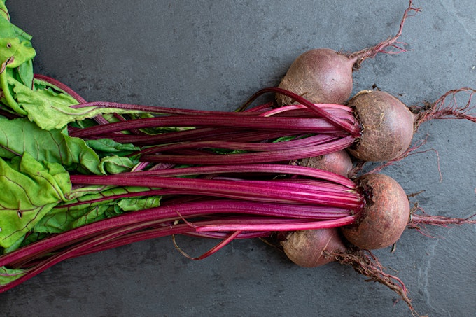A from-above image of bright magenta beets grouped together on a dark grey surface.