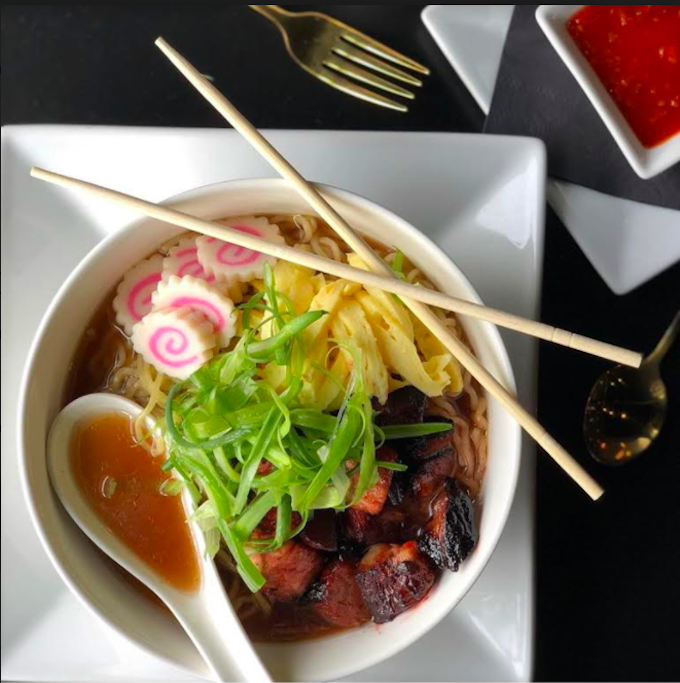 Looking down at a bowl of ramen with a spoon and chopsticks resting on the edge.