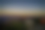 Looking out over a canyon with tall rocky mountains in the distance. They have flat tops and glow orange. The sky is blue fading into white, yellow, and orange.