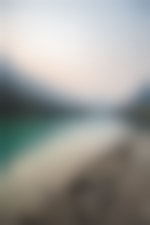 A clear lake reflects the mountains around the shorelines. Two people stand on a tall pier that juts out over the water.