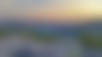 Rocky foreground overlooking a lush green mountainous landscape. Sky is a soft orange color at sunset.