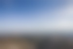 rocky mountain peaks cover the foreground and background. The sky is blue and a person is standing nearly out of visible range to the right. The sky is bright blue.