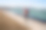 A person walks along a concrete path next to a teal lake with the Chicago skyline in the distance.