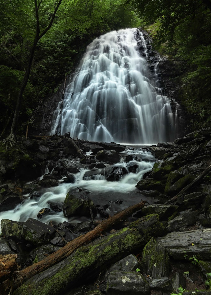 A tall waterfall cascades in many streams over a lot of rocks. Green trees surround the water.