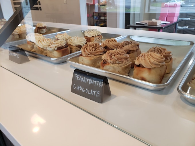 Looking into a bakery case at varieties of cinnamon rolls on silver baking trays.
