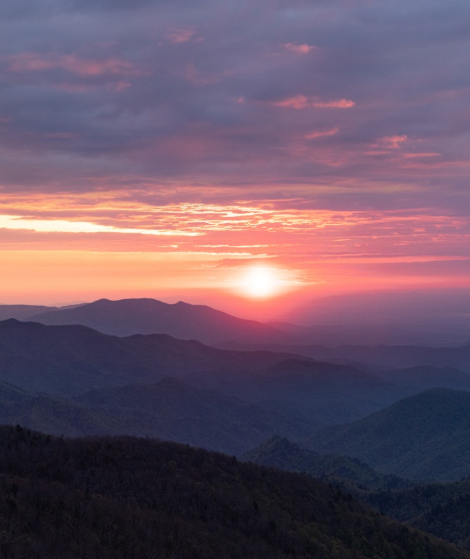 The sun is pink as it rises over purple mountains.