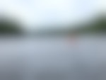 A person on a red kayak is floating on a lake with trees surrounding the shore.