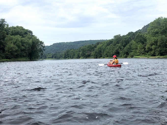 A person on a red kayak is floating on a lake with trees surrounding the shore.