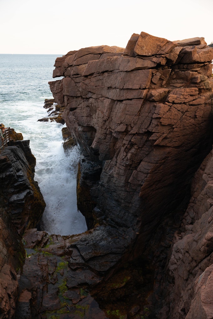A from-above view of a rocky area next to the ocean. The water is pouring into a deep hole between the rock walls.