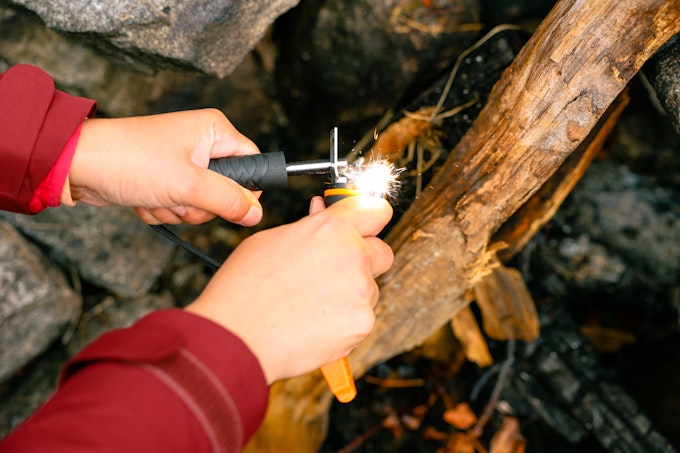 A close-up of a person with red sleeves using a fire striker to start a fire.
