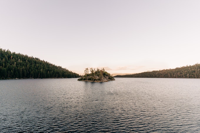 An island rests in the middle of a large body of water surrounded by trees.
