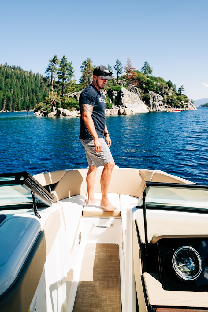A person is standing on the front of a boat on a body of water with an island in front of it.