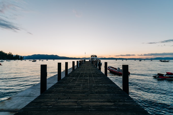 A pier leads out into a large body of water at sunset or sunrise.