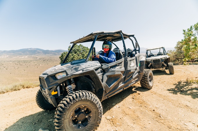 A person in a helmet and goggles is driving an off-road vehicle in sand.