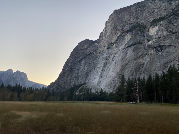 A tall rock mountain is surrounded by trees and a field.