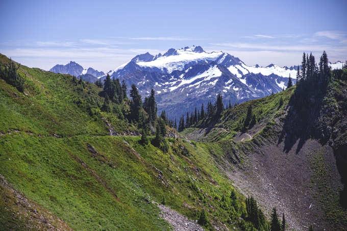 A green slope faces the camera while rocky, snowy peaks loom in the background.