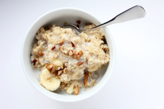 A from-above image of oatmeal with nuts and bananas in a white bowl. A spoon rests in the oatmeal.