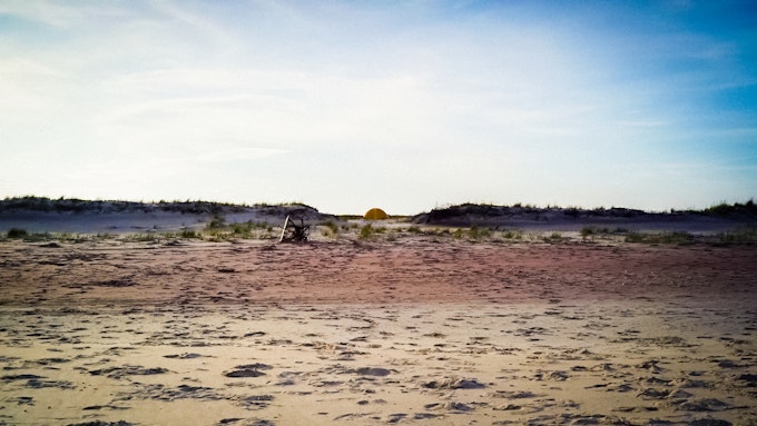 Sandy beach with beach grass and a tent in the distance on Watch Hill, Fire Island.