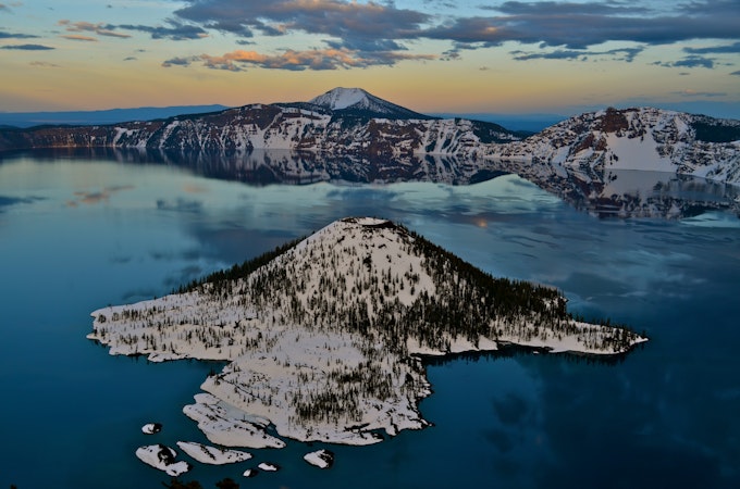 A snowy and pine forested island is surrounded by deep blue water