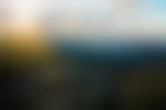 Looking out from a rocky area onto a series of sloping mountain peaks. The sun is peaking out behind clouds to the left, creating brilliant sunbeams that flow across the valley.