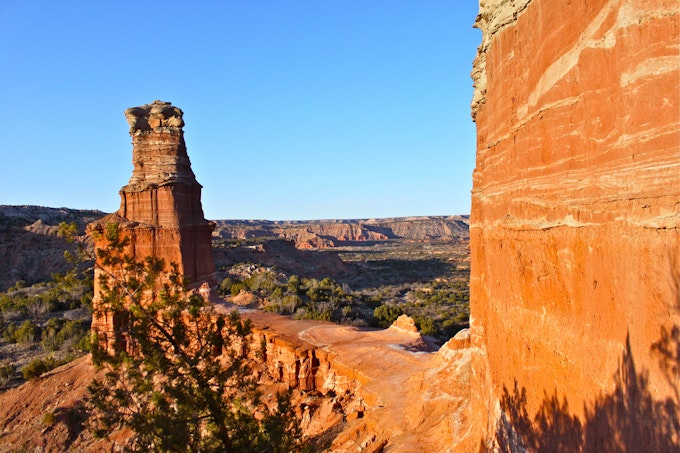 A tall red rock tower is at the end of a rock walkway looking out over a rocky valley.