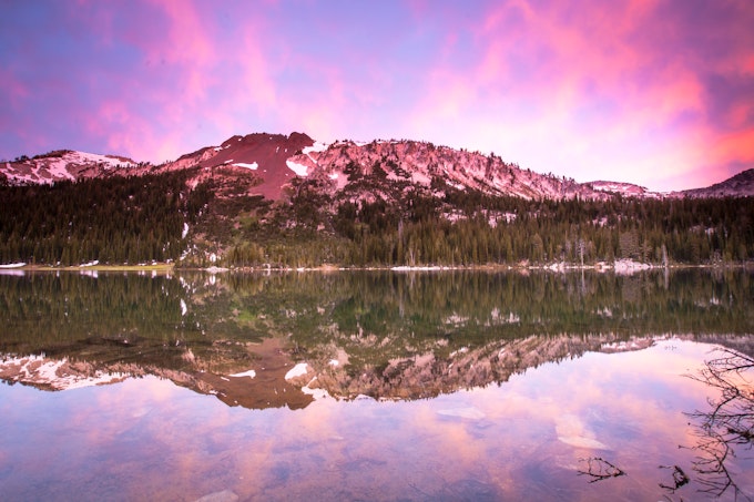 A glassy lake reflects the mountain and vibrant blue and pink sunset