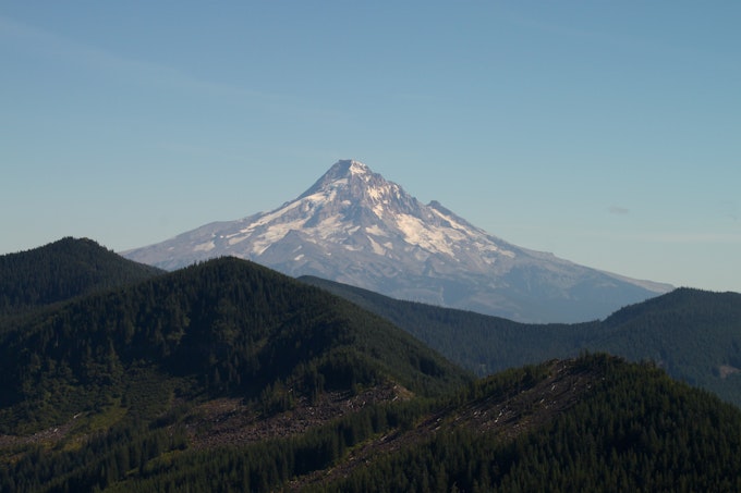 Mountain peaks are blanketed by green forests and Mount Hood shoots into the air in the background