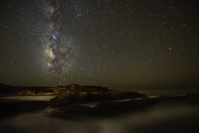 A peninsula is dark and the sky is bright with many stars and the Milky Way.