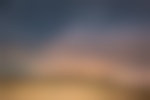 A person is standing on a sandy Texas hike with mountains far off in the distance. The sun is setting or rising and the sky is mostly navy blue with stars. There is orange and pink light coming up over the mountain.